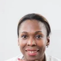 Close-up of a smiling woman with dark hair, wearing a white top, against a plain white background.