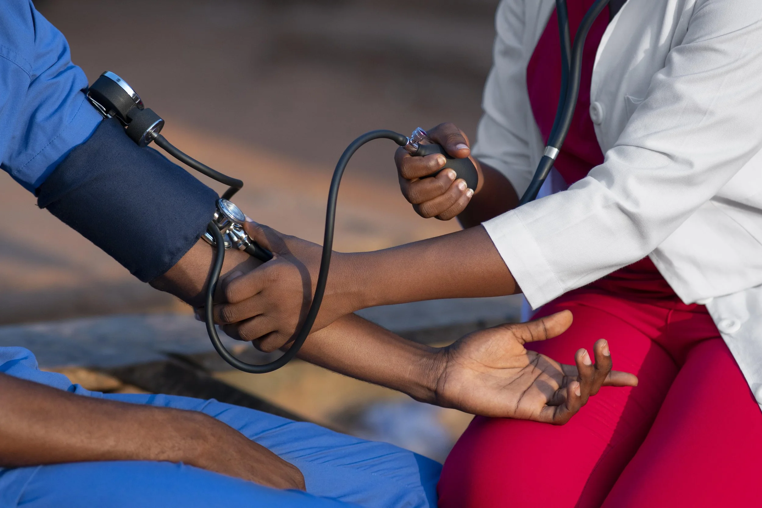 A healthcare professional checks a patient’s blood pressure with a sphygmomanometer, and the patient rests their arm on their lap.