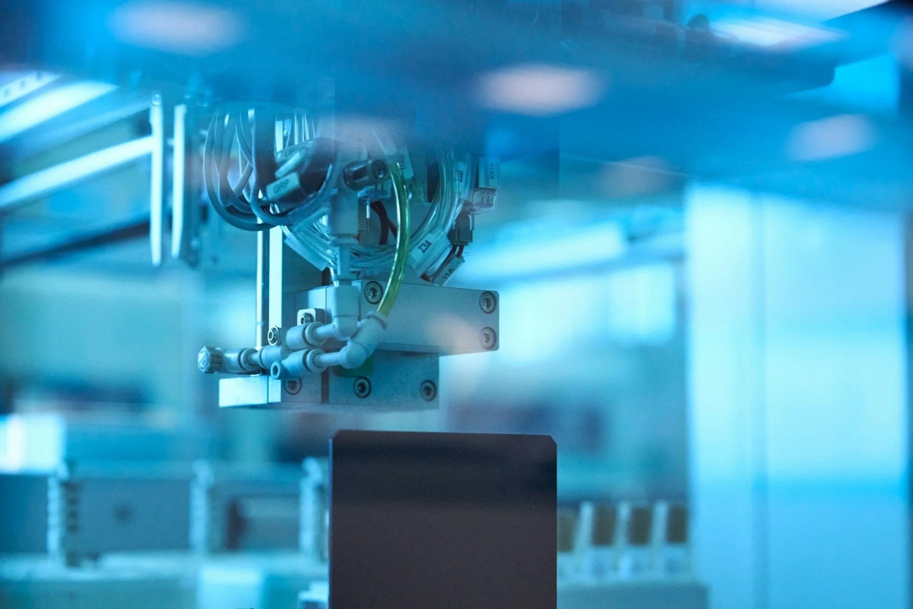 Close-up of a mechanical device with wires and tubing, inside a blue-tinted industrial or laboratory setting.