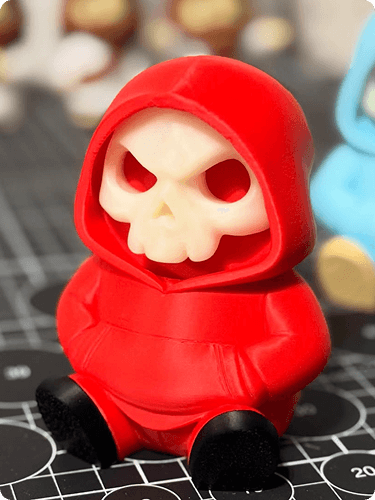 Red figurine of a skull with a hood, sitting on a cutting mat.