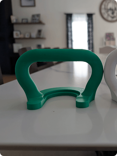 Green plastic handle or grip placed on a white surface in a room with shelves, pictures, and a window in the background.