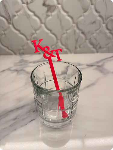 A clear glass of water with a red divider stick labeled 'K' and 'T' positioned inside it, on a marble countertop with a decorative tile backsplash in the background.