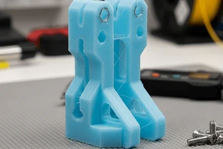 Blue 3D-printed object with a rectangular and angular shape on a workbench, surrounded by tools and screws 3d printed using PETG filament.