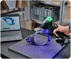 A person using a 3D scanner on a purple-colored object, with a laptop displaying a 3D model in the background.
