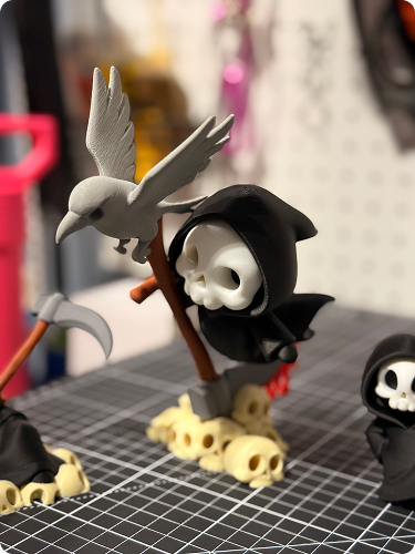 Decorative skeleton figure with a skull wearing a black hood, holding a staff, accompanied by a bird perched on the staff, placed on skulls.