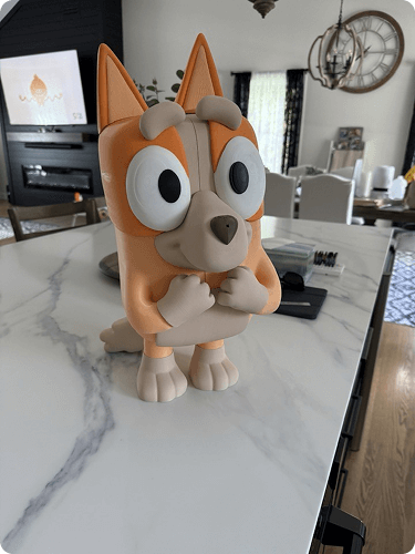 Cartoon-style figurine of a cute orange dog with big eyes, standing on a white marble kitchen countertop.