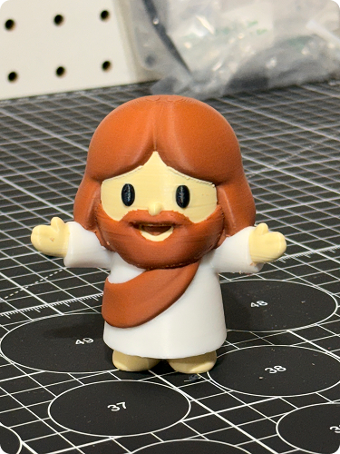 A small figurine of Jesus with brown hair and beard, wearing a white robe, standing on a black circular measuring mat.