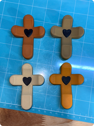 Four bandages shaped like crosses with black heart designs in the center, arranged on a blue grid surface.