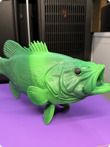 A green plastic fish-shaped object with a black eye resting on a purple surface.