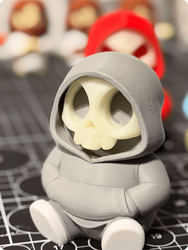 A small skeleton figurine wearing a hoodie and sitting with crossed arms, with other similar skeleton figures in the background.