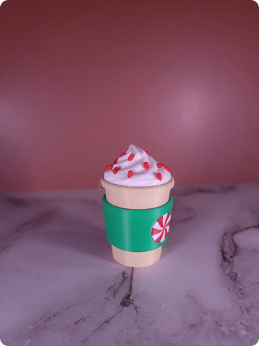 A small toy resembling a coffee cup with whipped cream and red sprinkles on top, placed on a marble surface.