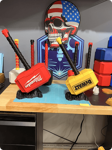 A display of toy hammers labeled Milwaukee and DeWalt in front of a skull with an American flag design and sunglasses, in a workshop or store setting.