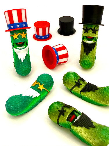 Various rubber toys shaped like pickles wearing patriotic hats and accessories, including Uncle Sam hats and black top hats, with some toys also sporting sunglasses and beards.