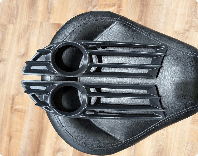 Two black plastic car vent louvers placed on a black leather cushioned surface, viewed from above.