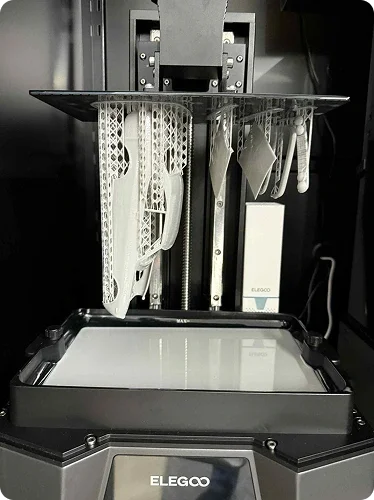3D printing machine with various plastic parts hanging from hooks.