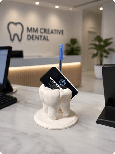 Tooth-shaped pen holder on a marble countertop at MM Creative Dental, with a toothbrush and dental office background.