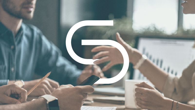 Who We Are: We work at every level: coaching individuals, developing teams, and facilitating organizational culture. Real transformation requires all three. [People in a business meeting with a laptop and documents on the table.]