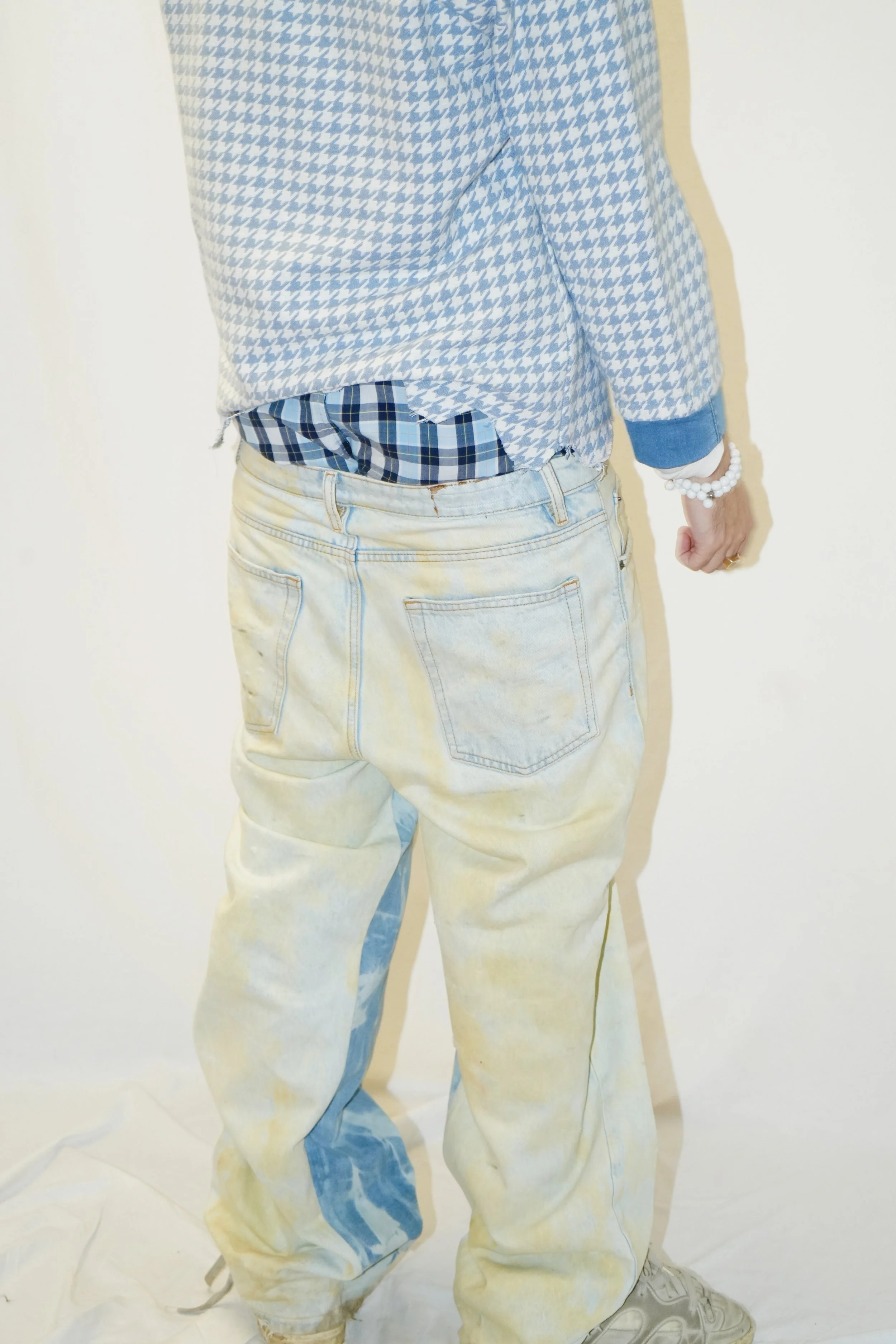 Vue de dos d'une personne portant un pantalon clair, une chemise à manches longues, des cravates bleu clair et blanches et un bracelet blanc au poignet droit.