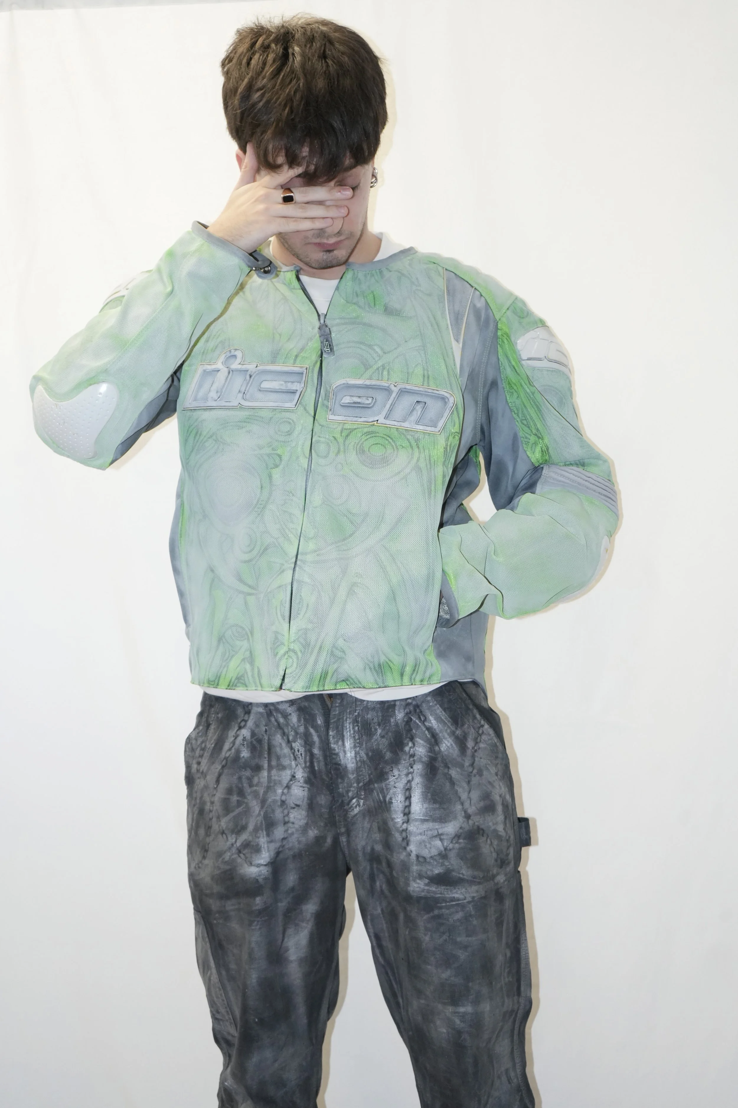 Garçon en tenue de motard, la main sur les yeux, sur fond blanc.