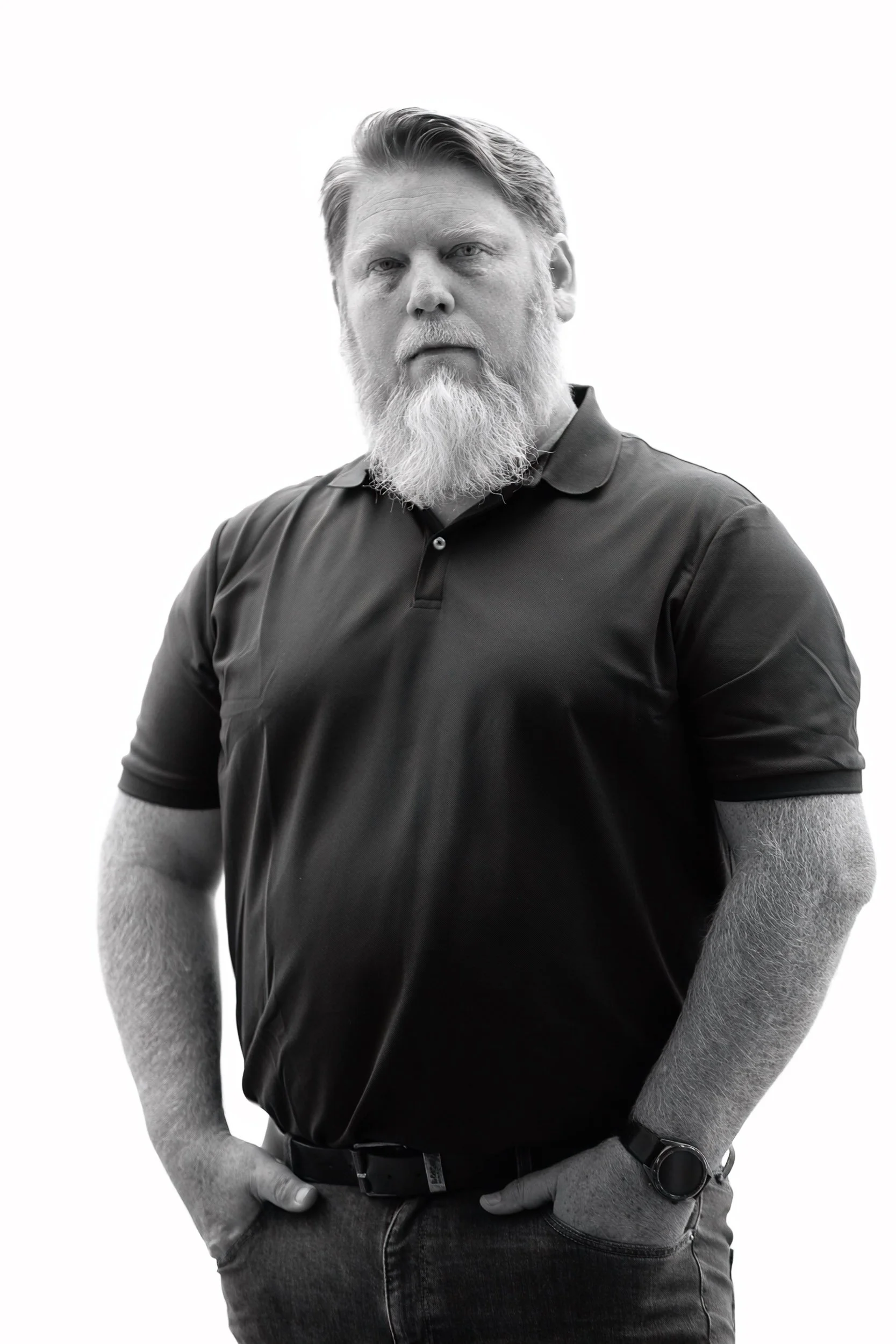 Black and white portrait of a middle-aged man with a beard, wearing a polo shirt and a wristwatch, with a serious expression.