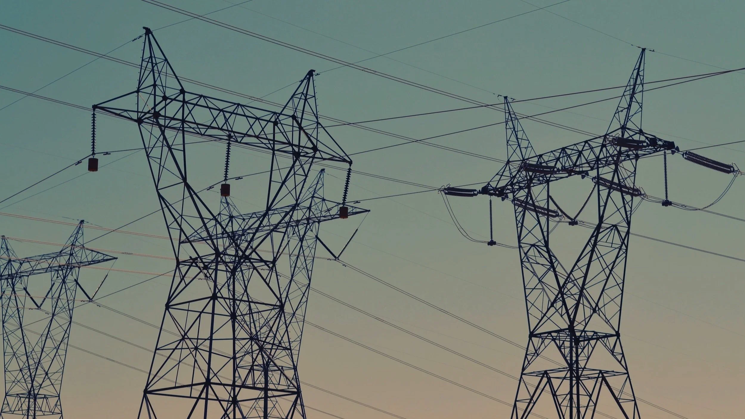 High-voltage power lines and transmission towers silhouetted against the sky at dusk.