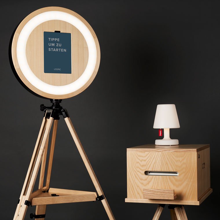 Ein Ringlicht auf einem Holstativ, das eine Anweisung zeigt, während ein kleiner Nachttisch mit einer Lampe darauf steht.