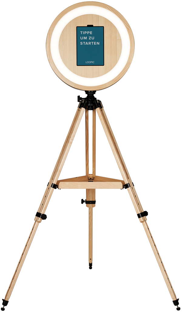 Ein Studioblitzlicht mit einem runden, beleuchteten Rahmen auf einem Holzstativ. Ein Tablet ist in der Mitte des Lichts montiert, mit dem Text: "TIPPE UM ZU STARTEN."