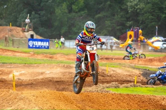 A motocross rider jumping over a dirt track at a race, wearing a helmet and colorful racing gear.