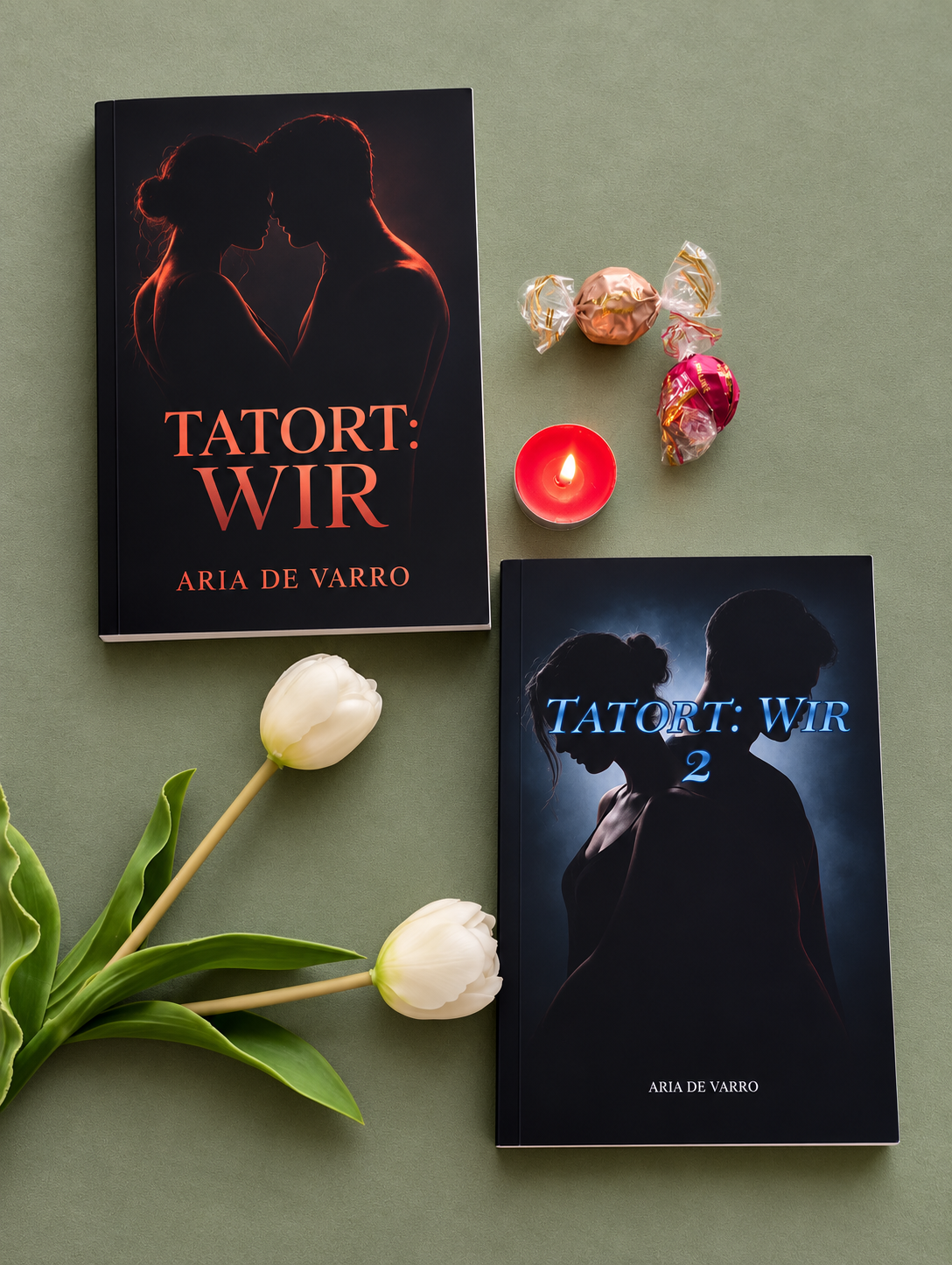 Zwei Bücher, ein Kerze, zwei Pralinen, zwei weißen Tulpen auf einem grünen Hintergrund. Das Buch oben ist schwarz mit roten Silhouetten eines Paares und dem Titel "Tatort: Wir" von Aria de Varro. Das Buch unten ist schwarz mit blauer Schrift und Silhouette eines Paares, mit dem Titel "Tatort: Wir 2" von Aria de Varro.