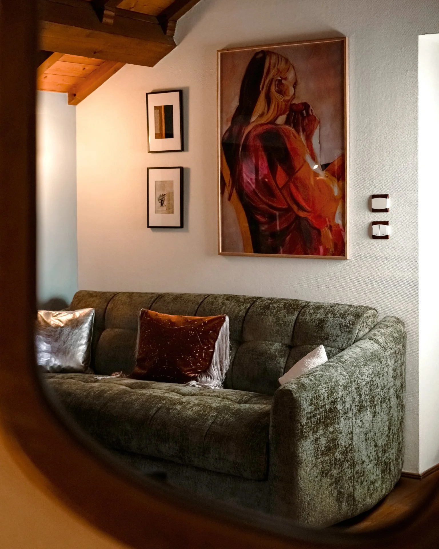 Un canapé en tissu vert foncé dans un salon avec des coussins en velours, des œuvres d'art encadrées sur le mur, et une lumière douce.