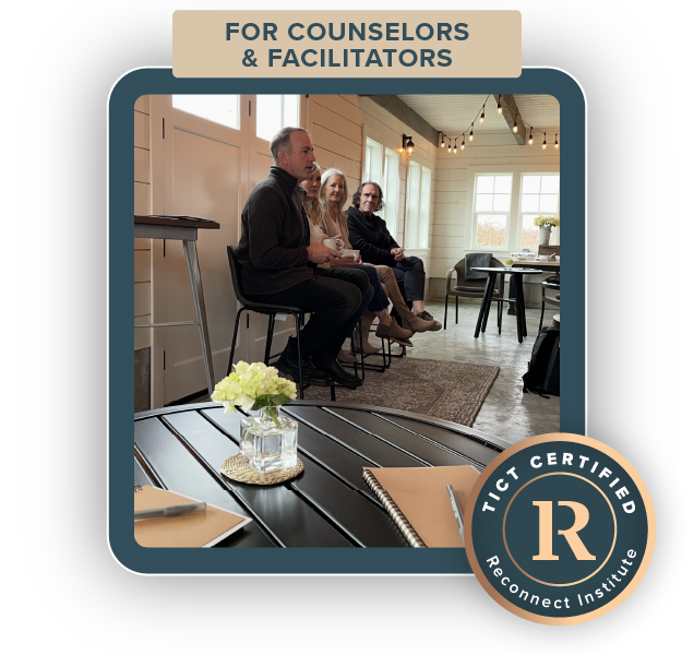 Counselors and facilitators seated on chairs during a workshop or seminar in a bright, modern room with large windows and string lights, with a table in the foreground holding a flower arrangement and notebooks.