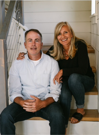 A man and a woman sitting on wooden stairs inside a house, smiling at the camera.