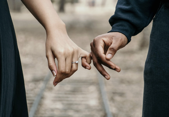 Close-up of a couple holding hands, with a train track in the background.
