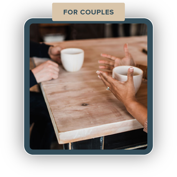 Two people sitting at a wooden table, each holding a white mug, engaging in conversation with the focus on their hands. The image is labeled "For Couples" at the top.