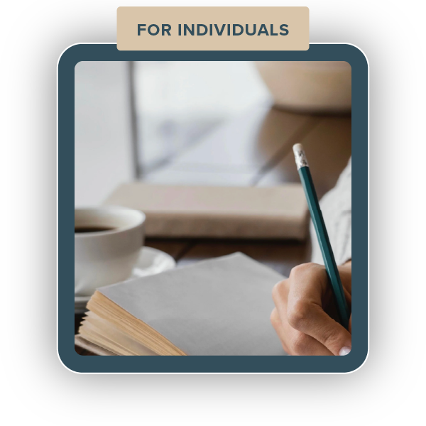 A person writing in a notebook with a pencil, with a cup of coffee and a laptop on a desk, and a sign that reads 'For Individuals' at the top