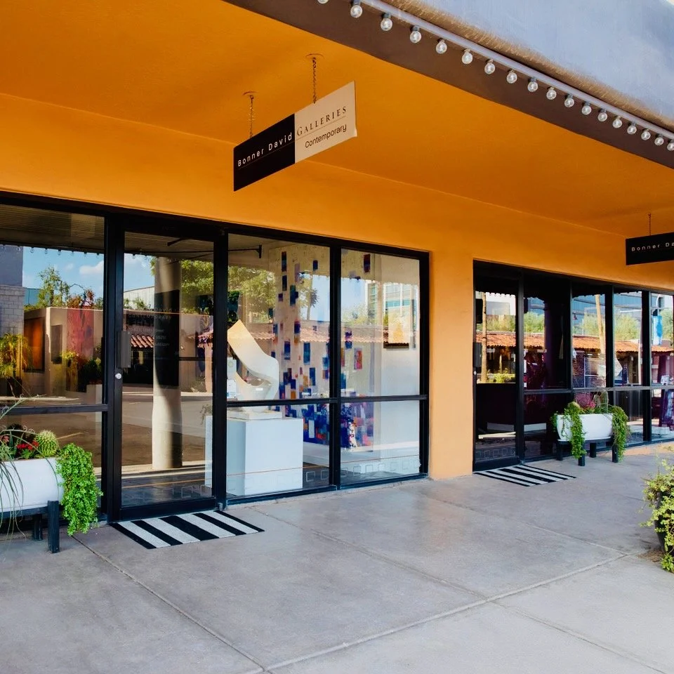 Exterior of an art gallery with large glass windows, potted plants outside, and signs indicating it is Bonner David Galleries, a contemporary art gallery.
