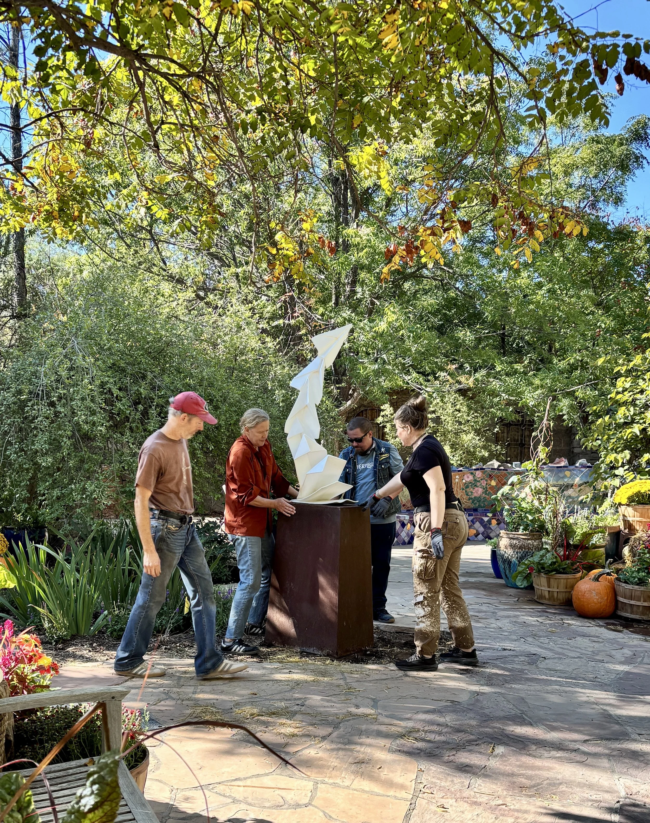 Box Studio teammates and ABQ BioPark staff install a tall, white metal abstract sculpture of a paper plane called Folding Planes by Kevin Box.
