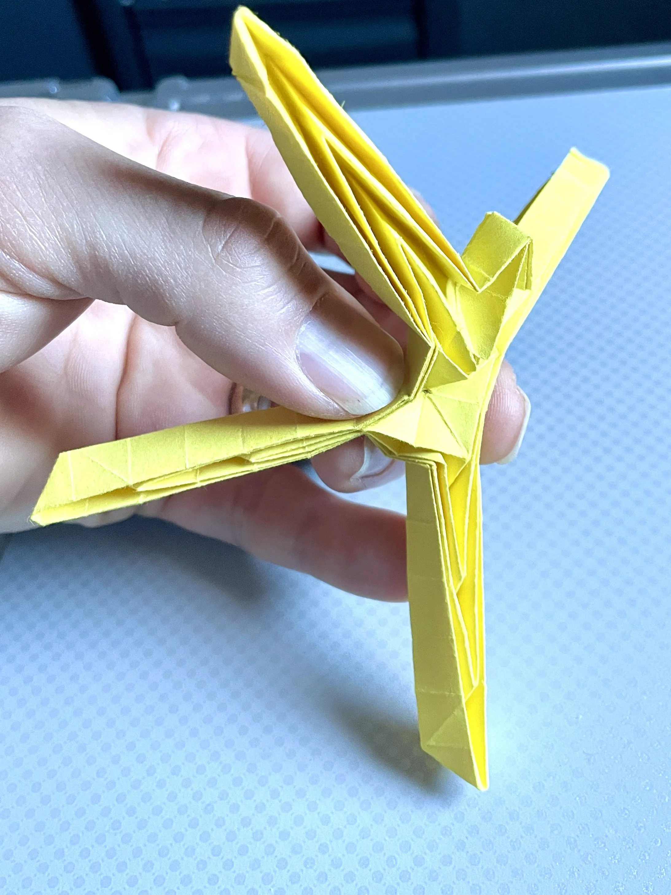 Close-up of a yellow origami butterfly held by a person's hand against a blue background.