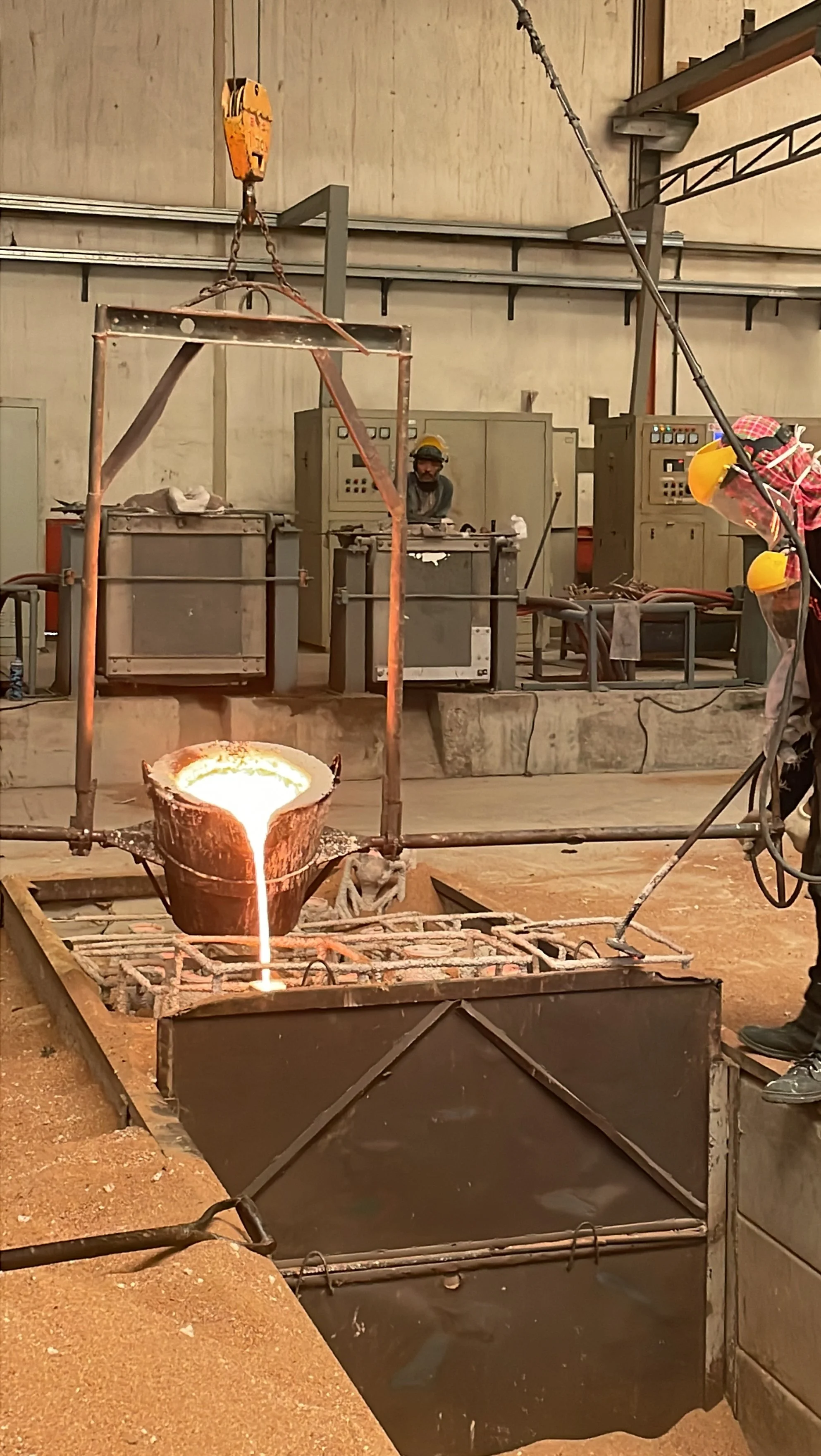 Futuristic industrial scene with molten metal pouring from a crucible into a mold, with a worker in safety gear and machinery in the background.