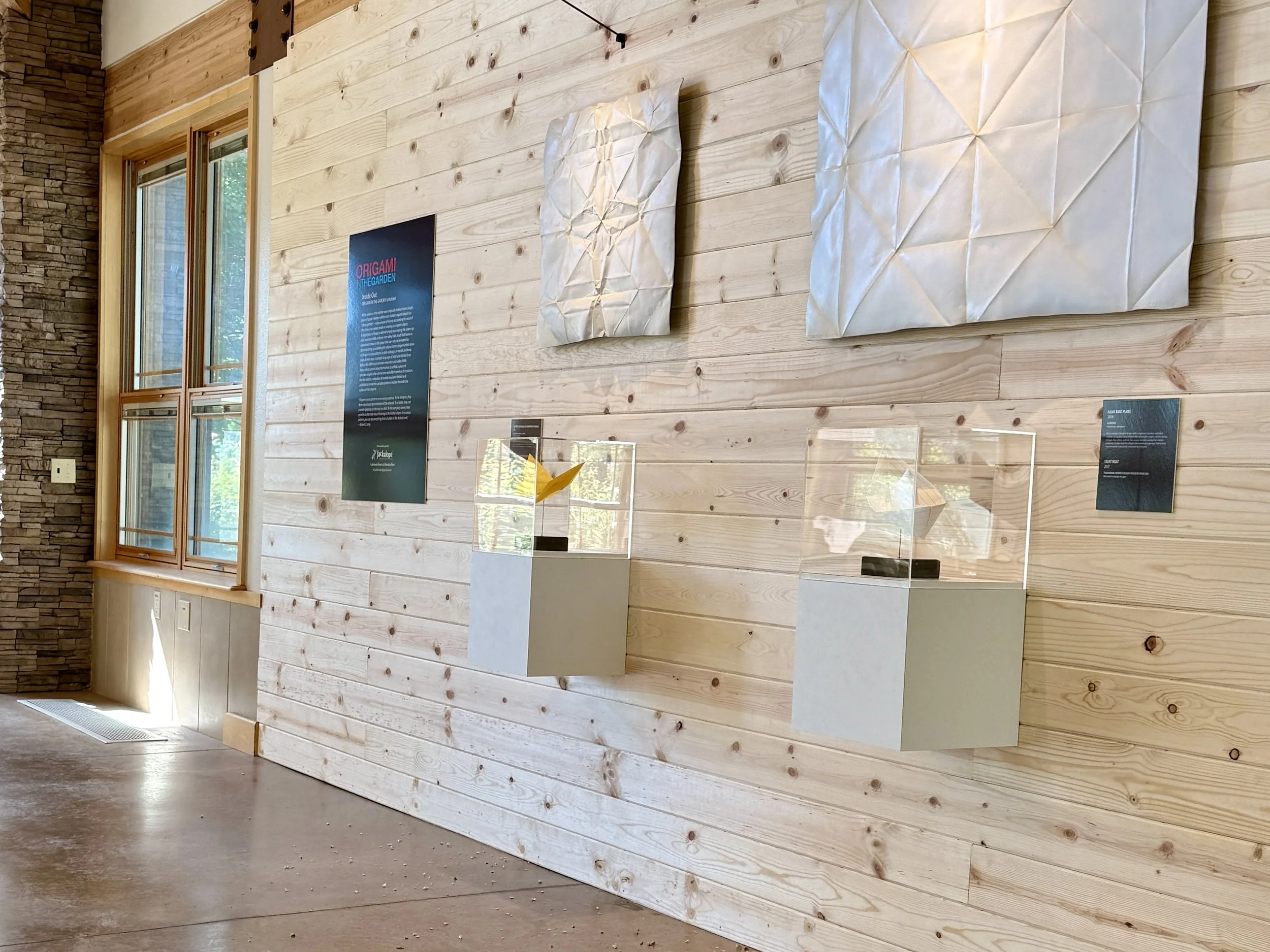 Paper origami models are displayed with cast metal unfolded origami patterns as part of the Inside Out display at the ABQ BioPark Botanic Garden.