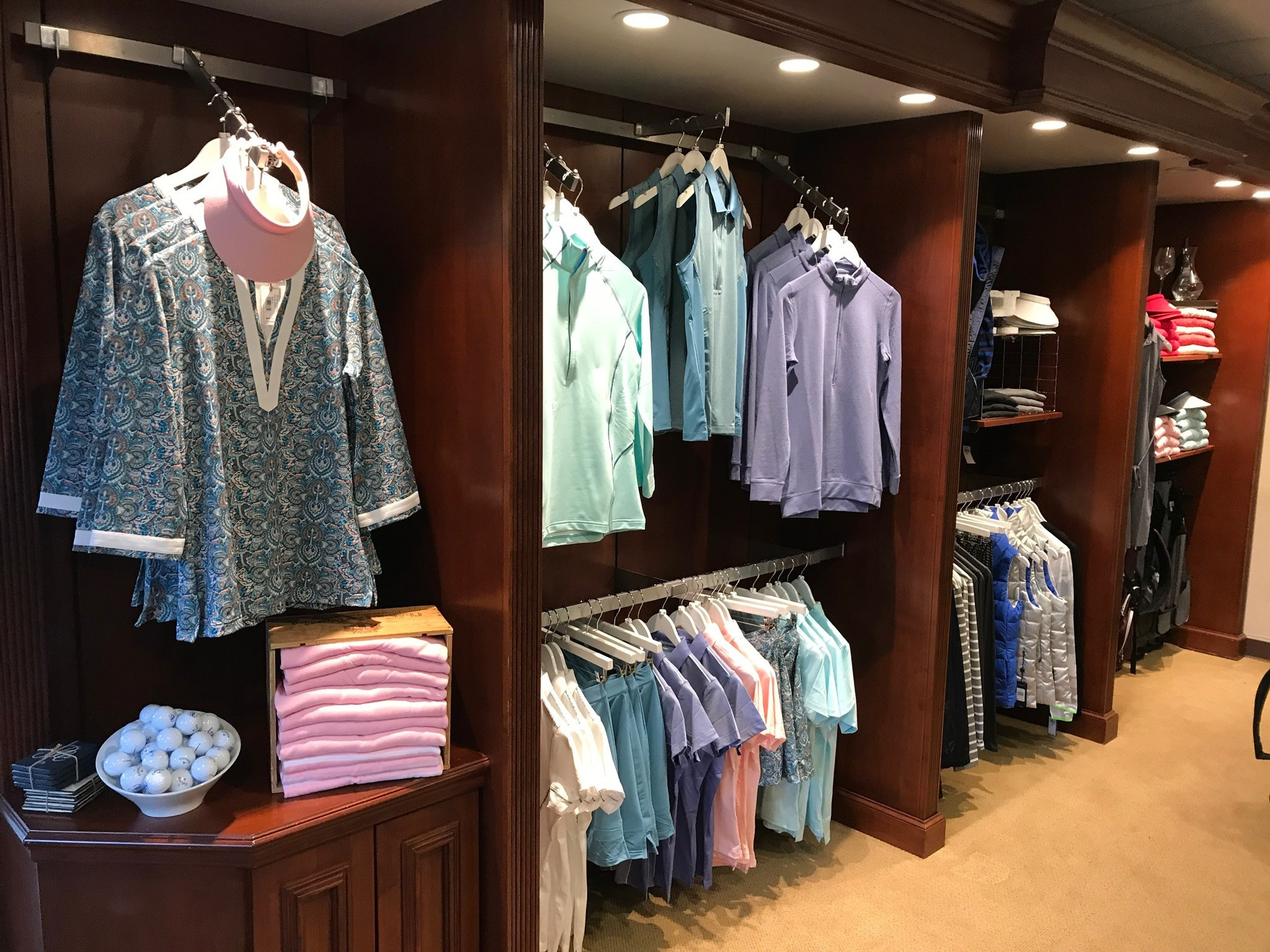 Clothing display with men's and women's shirts, sweaters, and accessories on wooden shelves in a retail store.