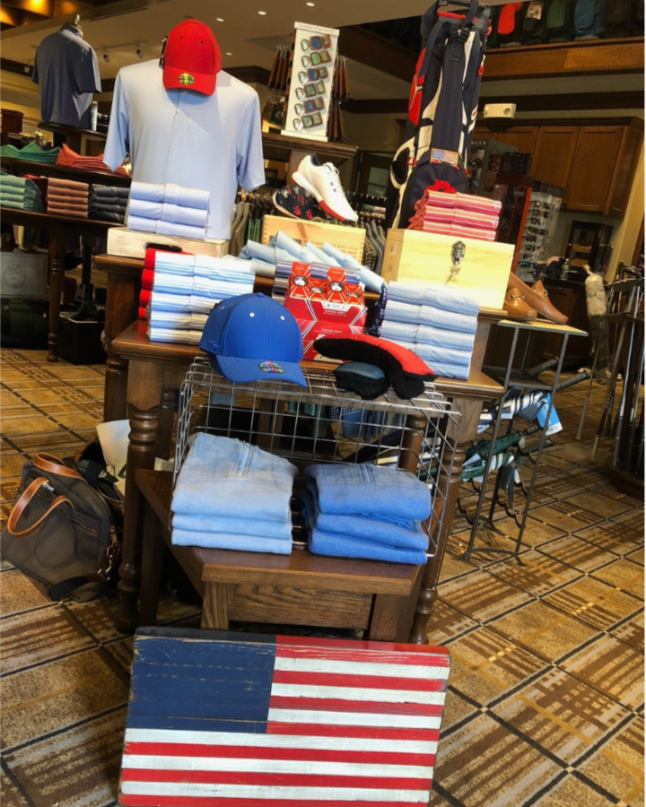 Display of golf accessories and apparel, including hats, golf gloves, towels, and shoes, with an American flag-themed decoration in the foreground at a golf shop.