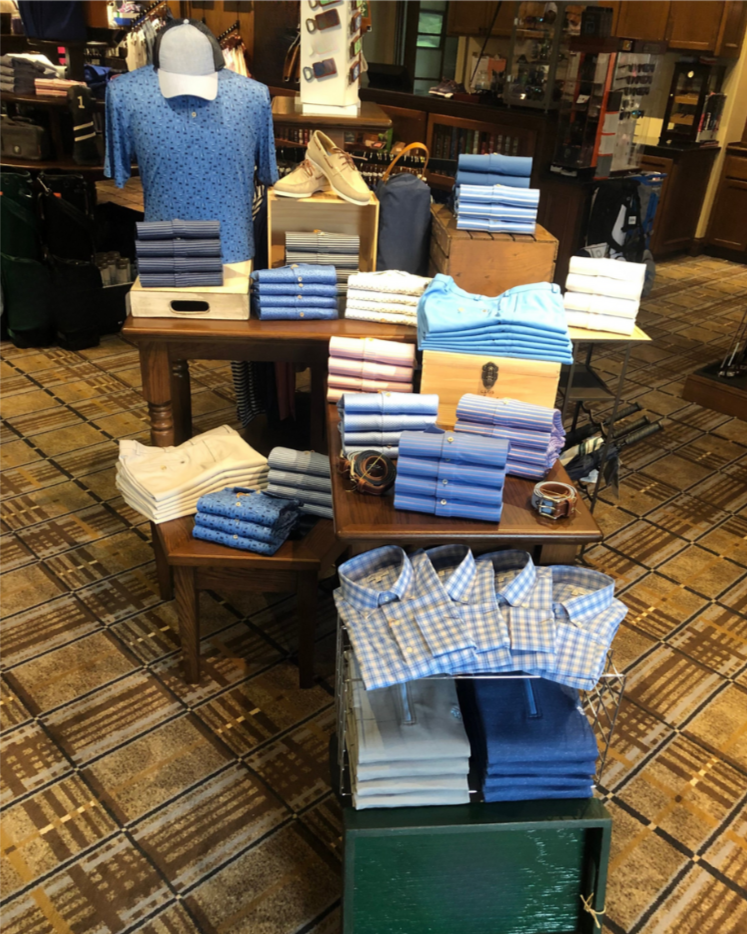 Display of men's Clothing and accessories in a store, including folded shirts, belts, and a mannequin wearing a blue shirt.