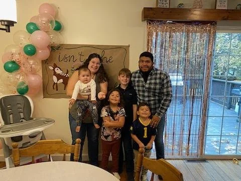 Jessica standing on the left holding her youngest child, three other children stand between her and her husband, Leo.