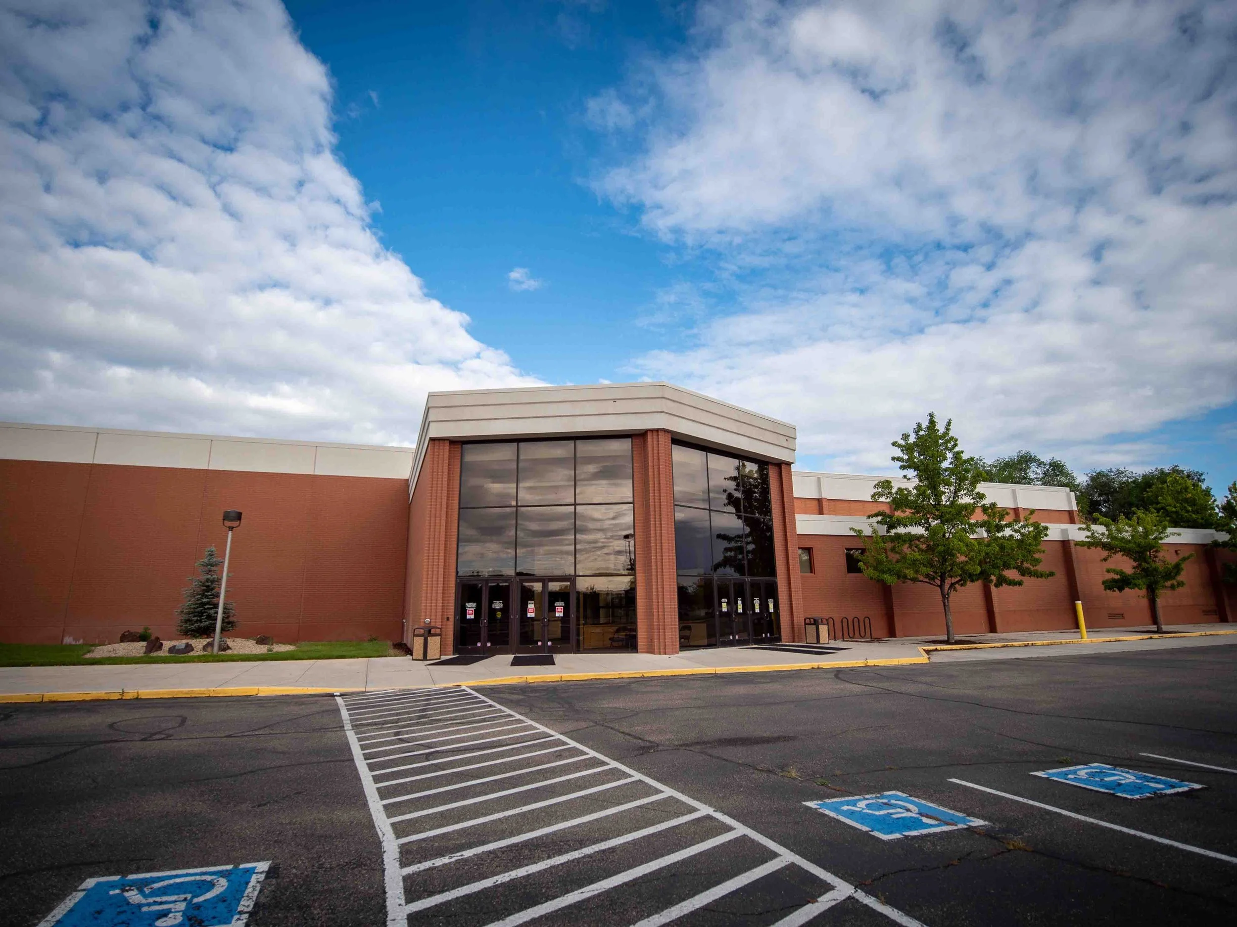 Empty parking lot with handicapped parking spaces and a shopping mall entrance under a partly cloudy sky.