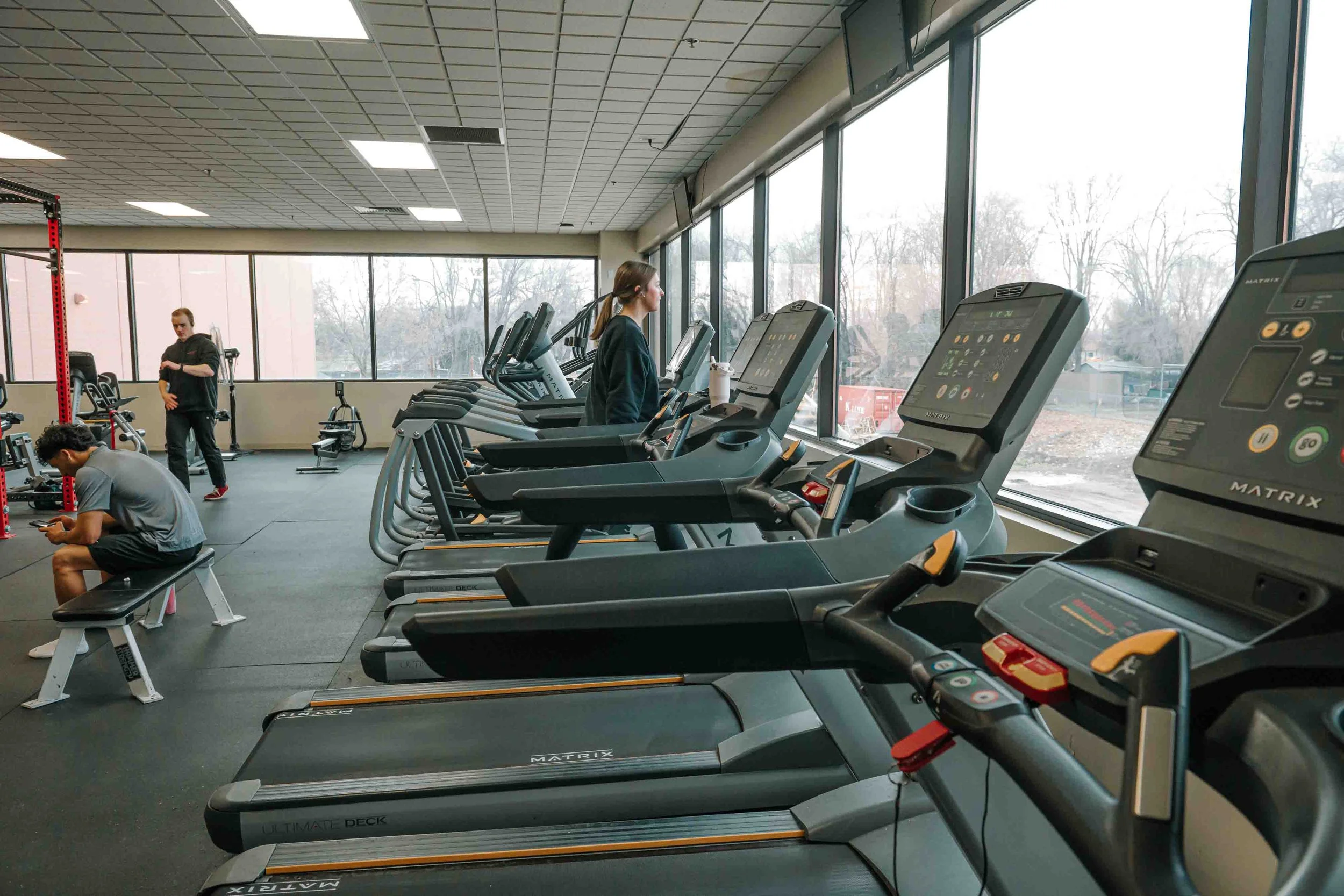 People working out on treadmills in a gym with large windows showing outdoor scenery