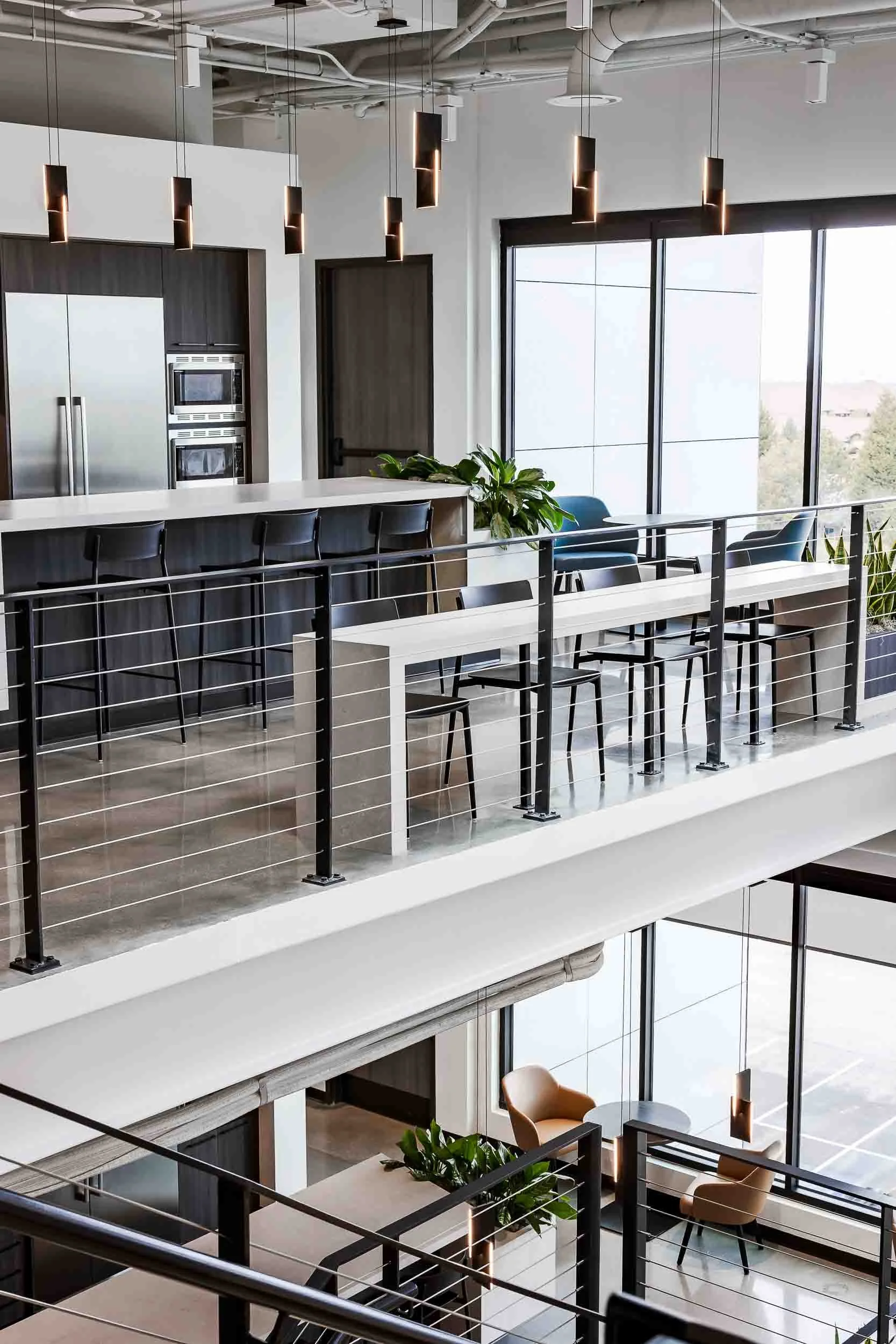 Interior view of a modern, multi-level office space with large windows, a kitchen area with bar stools, and a seating area with chairs and tables.