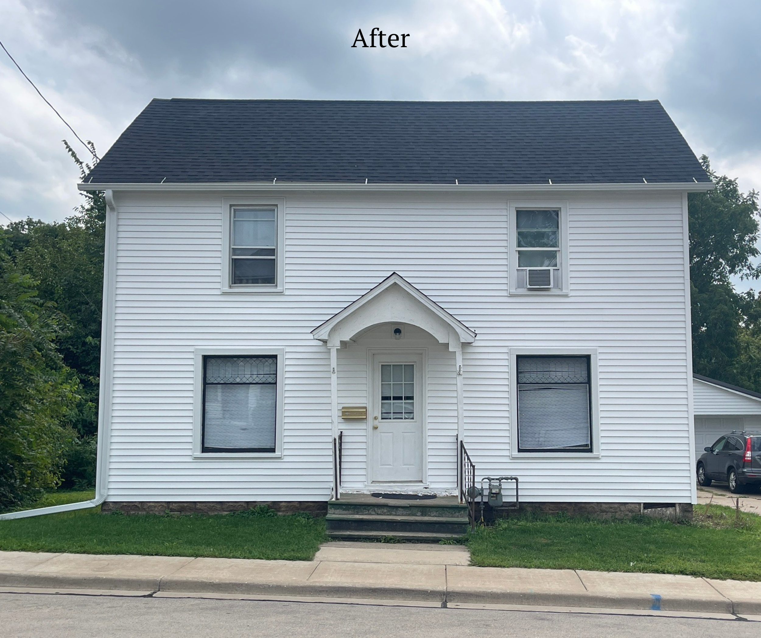 A two-story white house with a dark roof, four windows with blinds, a small porch with steps, and a front door. A black car is parked in the driveway to the right. The word 'After' is written at the top of the image.