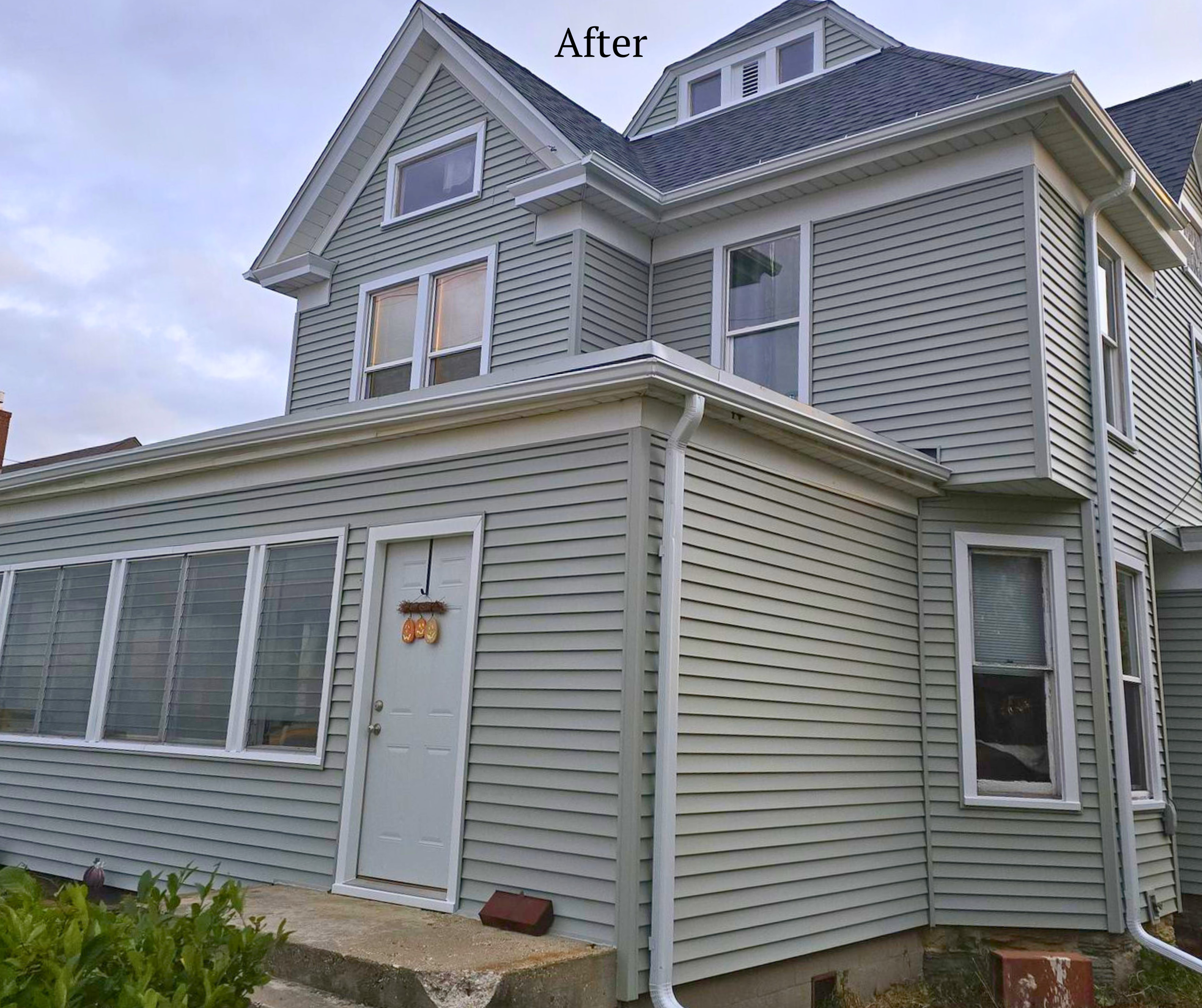 The house has fresh light green siding with white trim, multiple windows, and a white door with pumpkin and fall decorations, after renovation.