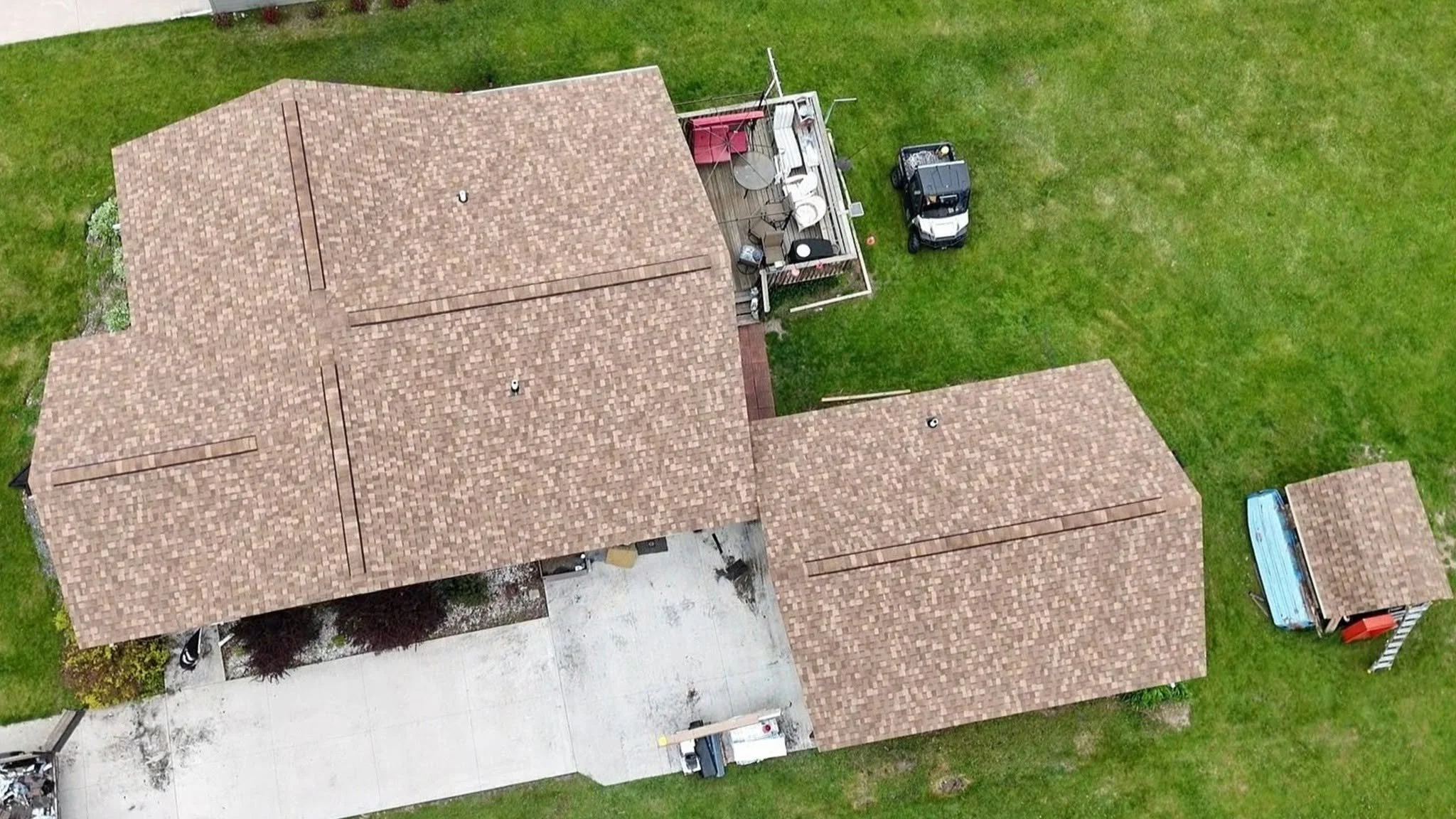Aerial view of residential houses with red tile roofs, green lawns, and driveways, including a golf cart parked on the grass.